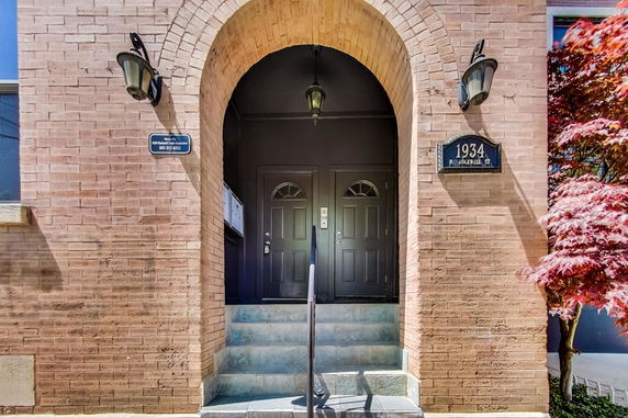 Front view of a building entrance with double black doors and a brick archway.