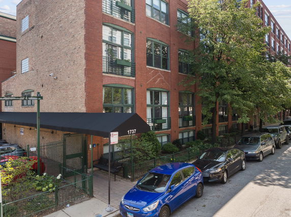 Front view of a multi-story brick building with large windows and a black awning at the entrance.