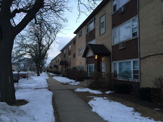 Front view of a multi-story apartment building with brick facade and snow on the ground.