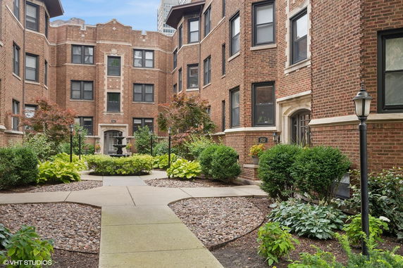 Front view of a brick apartment building with a landscaped courtyard and central fountain.