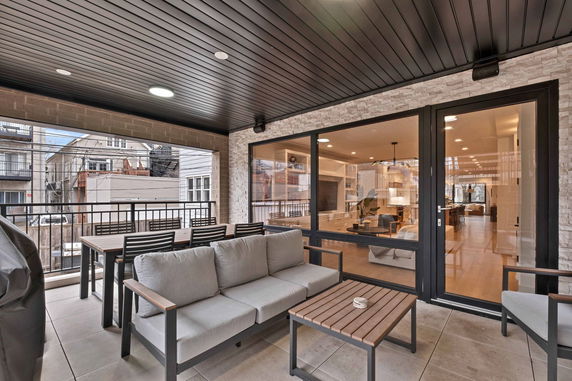 Covered patio area with outdoor furniture and a view of adjacent buildings.