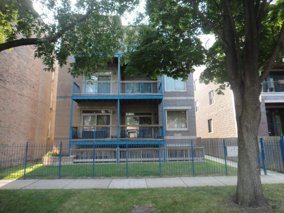 Front view of a multi-story apartment building with balconies and a metal fence.