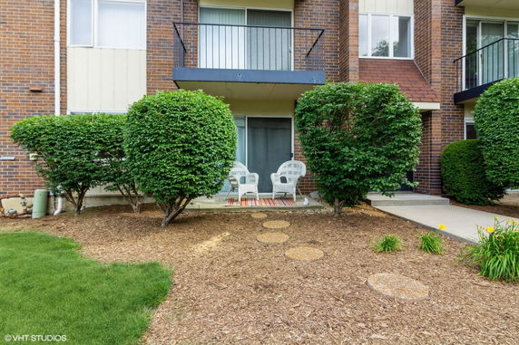Front view of a residential building with a small patio area and shrubbery.