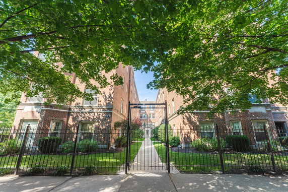 Front view of a brick apartment building with a walkway and gated entrance.
