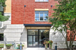 Front view of a brick apartment building with a glass entrance and potted plants.