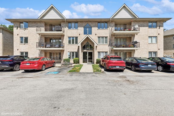 Front view of a three-story apartment building with balconies and parking area.