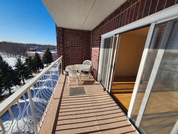 View from a balcony with a white railing, overlooking a snowy landscape and trees.