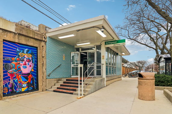 Entrance view of a public transit station with steps, glass doors, and a mural on the side wall.
