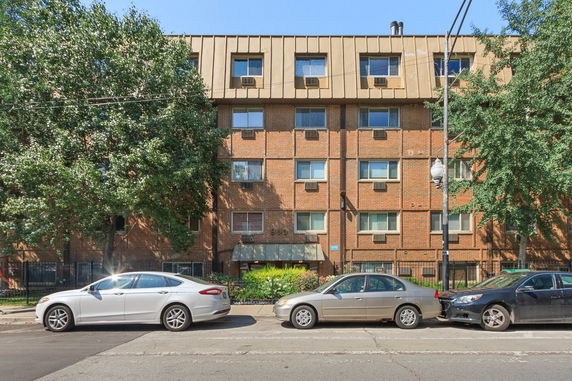 Front view of a multi-story brick building with multiple windows and air conditioning units.