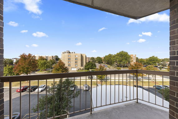 View from a balcony overlooking surrounding buildings and a parking area.