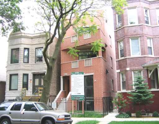 Front view of a multi-story brick building with adjacent residential structures.