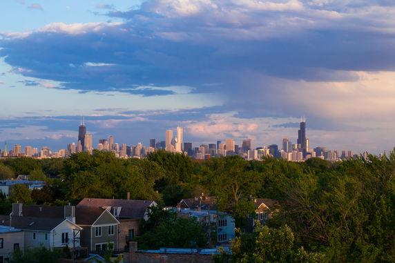 Wide view of a city skyline with skyscrapers and cloudy sky.