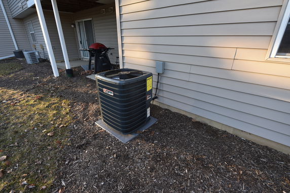 Outdoor view of a house with siding, air conditioning unit, and grill on a small patio.