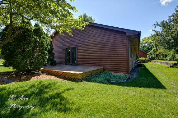 Side view of a one-story house with wooden siding and a small deck.