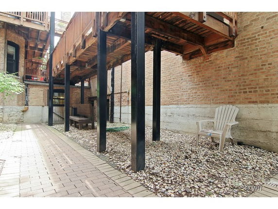 Outdoor area beneath elevated wooden deck with brick and concrete surroundings.