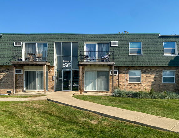 Front view of a two-story apartment building with balconies and green roof shingles.
