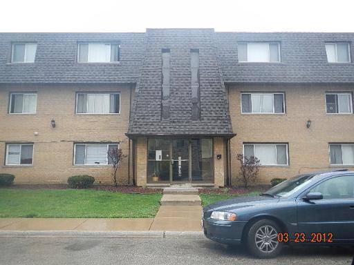 Front view of a three-story residential building with brick facade and shingled roof.