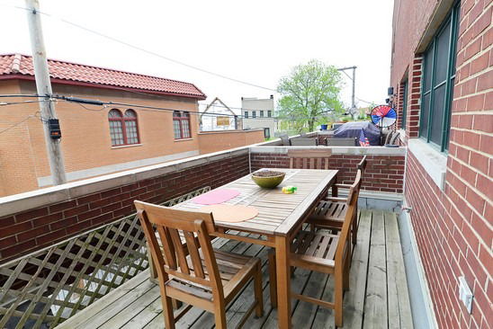 A rooftop area with a wooden dining table and chairs, featuring surrounding buildings in the view.