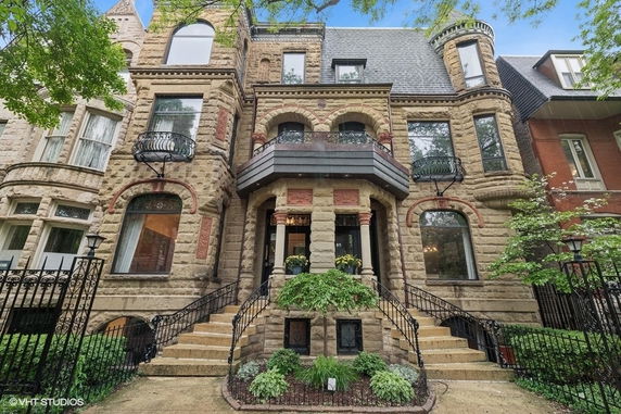 Front view of a historic multi-story stone house with decorative balconies and arched windows.