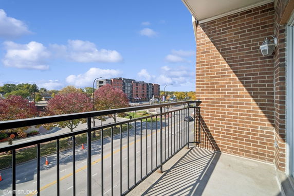 View from a balcony overlooking a road with trees and a distant multi-story building.