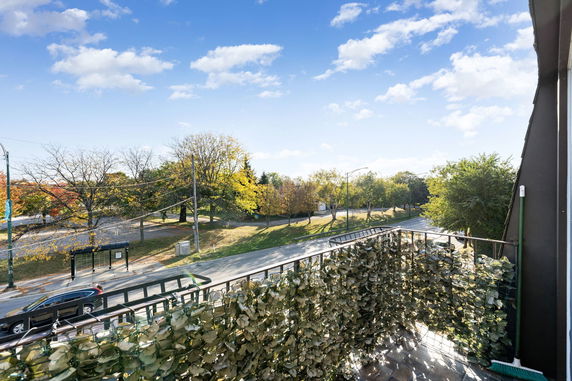 Panoramic view from a balcony showing a street and leafy trees under a clear blue sky.