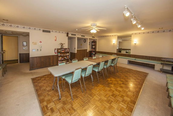 Interior view of a clubhouse room with a long table and chairs, surrounded by wood paneling and decorated with lights.