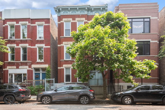 Front view of a red brick multi-story residential building with white window frames and decorative trim.