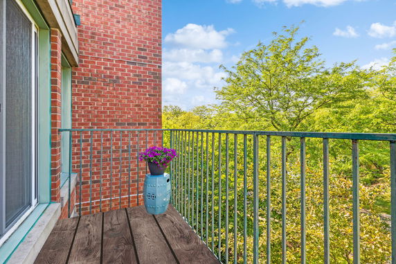 Exterior balcony with railing overlooking greenery and trees.