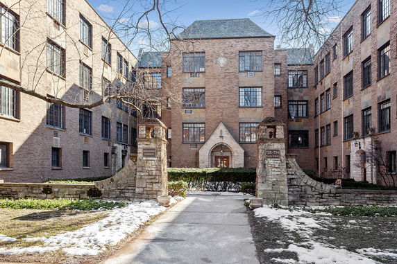 Front view of a multi-story brick apartment building with an arched entrance.