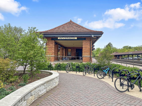 Front view of a brick building with a sloped roof named Riverside, surrounded by greenery and a bike rack.