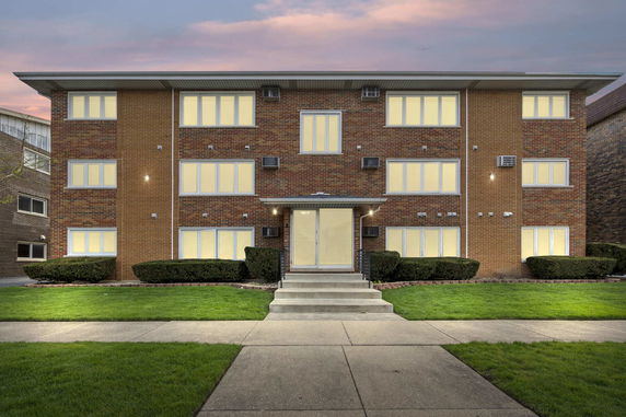 Front view of a three-story brick building with illuminated windows and a central entrance.