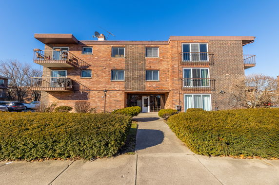 Front view of a three-story brick apartment building with balconies.