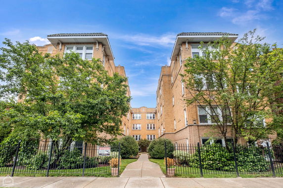 Front view of a multi-story brick apartment building with a gated entrance.