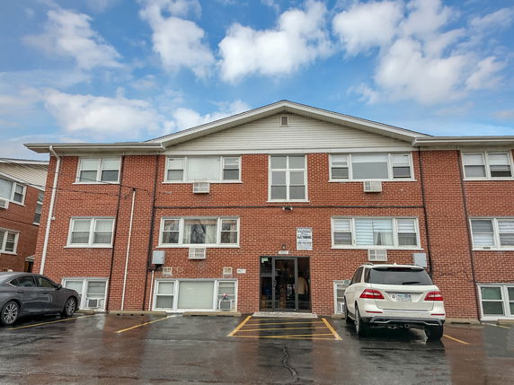 Front view of a two-story brick apartment building with a parking lot.