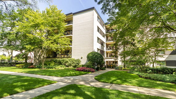 Front view of a multi-story apartment building with balconies and landscaped surroundings.