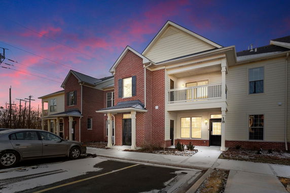 Front view of a two-story building with brick and siding exterior, featuring balconies and parking spaces.