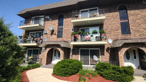 Front view of a three-story brick apartment building with balconies.