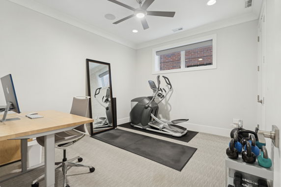 Room with exercise equipment including an elliptical machine, kettlebells, desk, and chair.