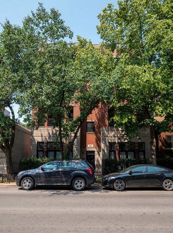 Front view of a brick multi-story building with trees and parked cars in front.