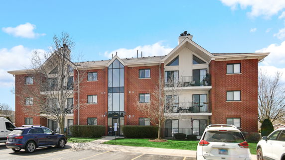 Front view of a three-story brick apartment building with balconies and a central glass entrance.