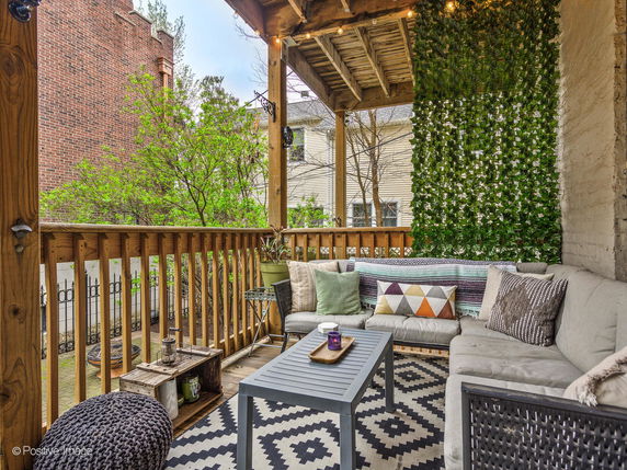 Outdoor sitting area on a wooden porch with decorative pillows and vibrant plants.