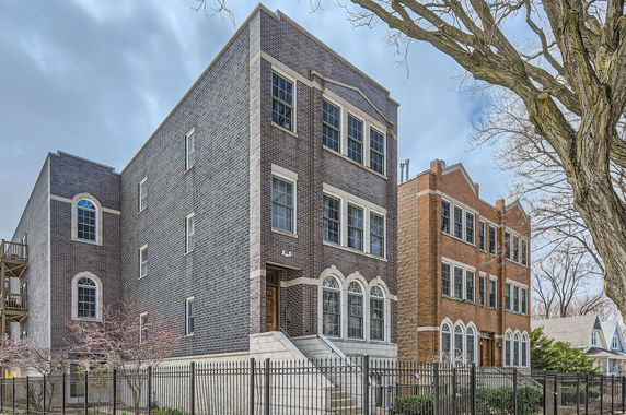 Front view of a three-story brick building with large windows and a gated entrance.