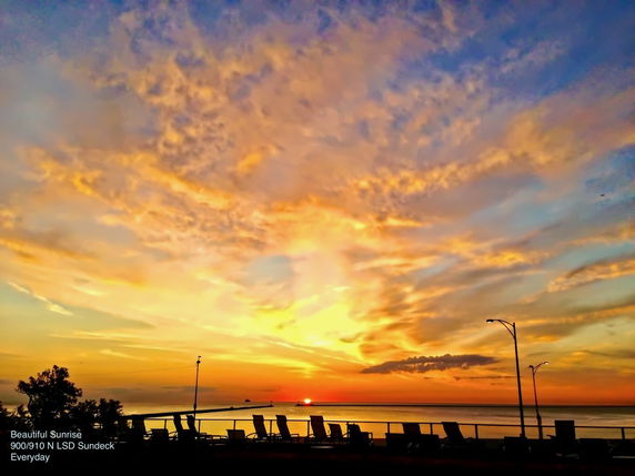 Panoramic view of sunrise over the ocean with lounge chairs silhouetted in the foreground.