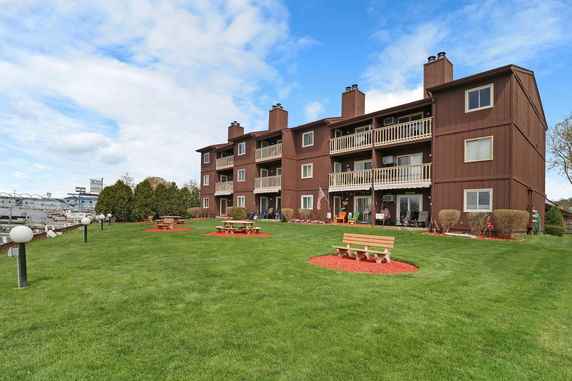 Front view of a three-story building with balconies overlooking a grassy area with benches.