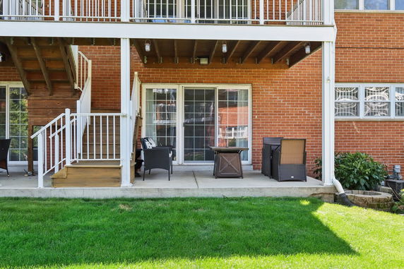 Rear view of a two-story house with a patio and staircase leading to an elevated deck.