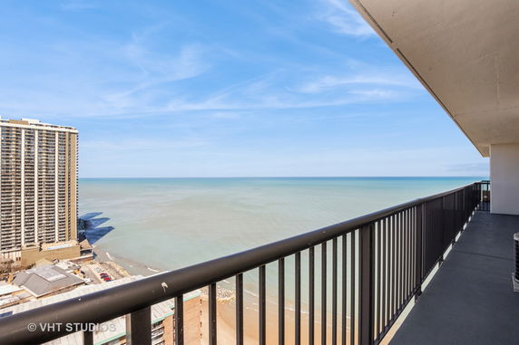 Wide angle view from a high-rise balcony overlooking the ocean and adjacent buildings.