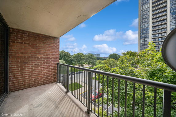 View from a balcony overlooking a grassy area with trees and a tall building in the background.