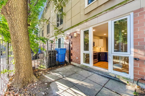 Rear view of a multi-story building with a patio and open door to a kitchen.
