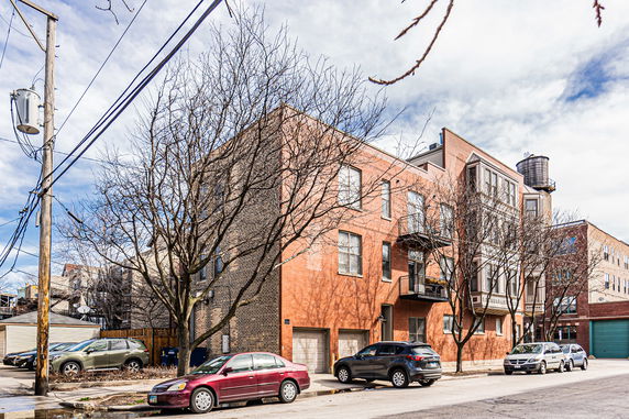 Front view of a multi-story brick building with cars parked in front.