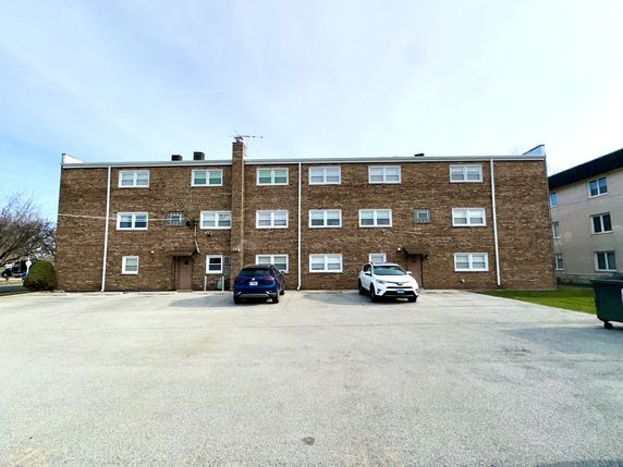 Front view of a three-story brick apartment building with parking area.